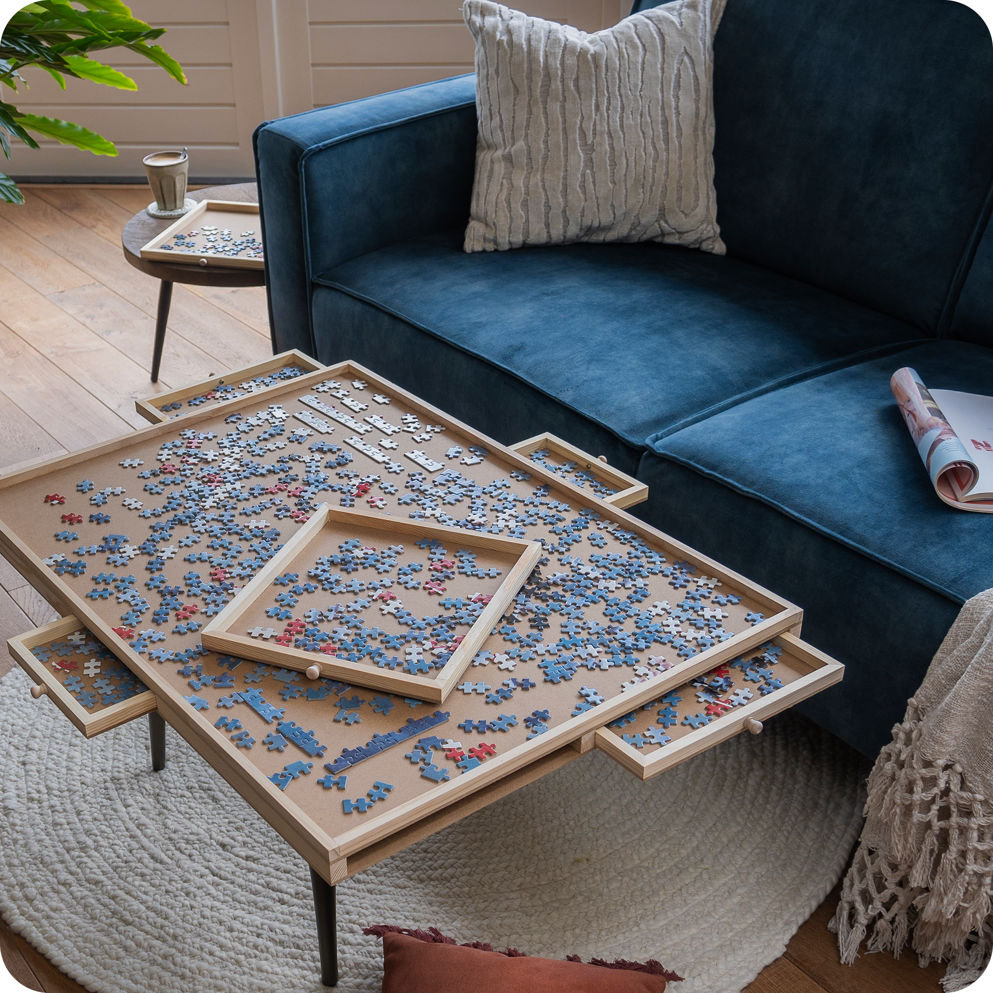 Een landelijke woonkamer met een blauwe bank en landelijke decoratie. Op de salontafel staat een puzzelplaat met een puzzel van 1500 stukjes erop. De lades zijn uitgeschoven en ook gevuld met puzzelstukjes.